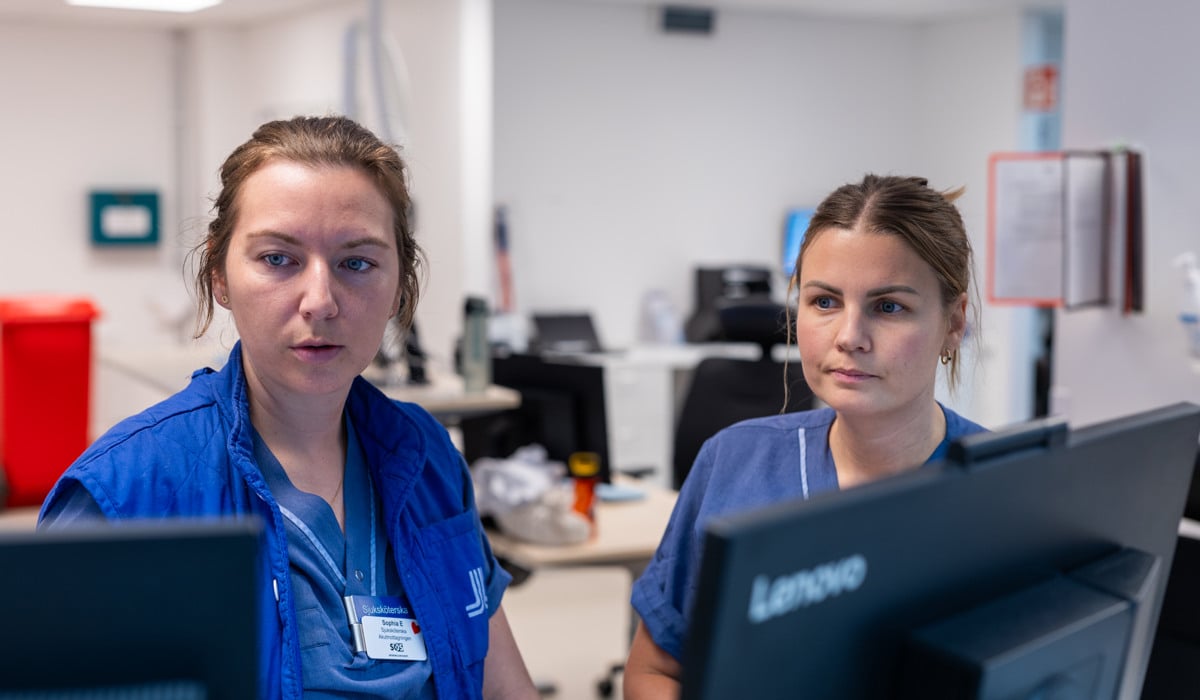 Två kvinnor som arbetar inom vården står framför datorer.
